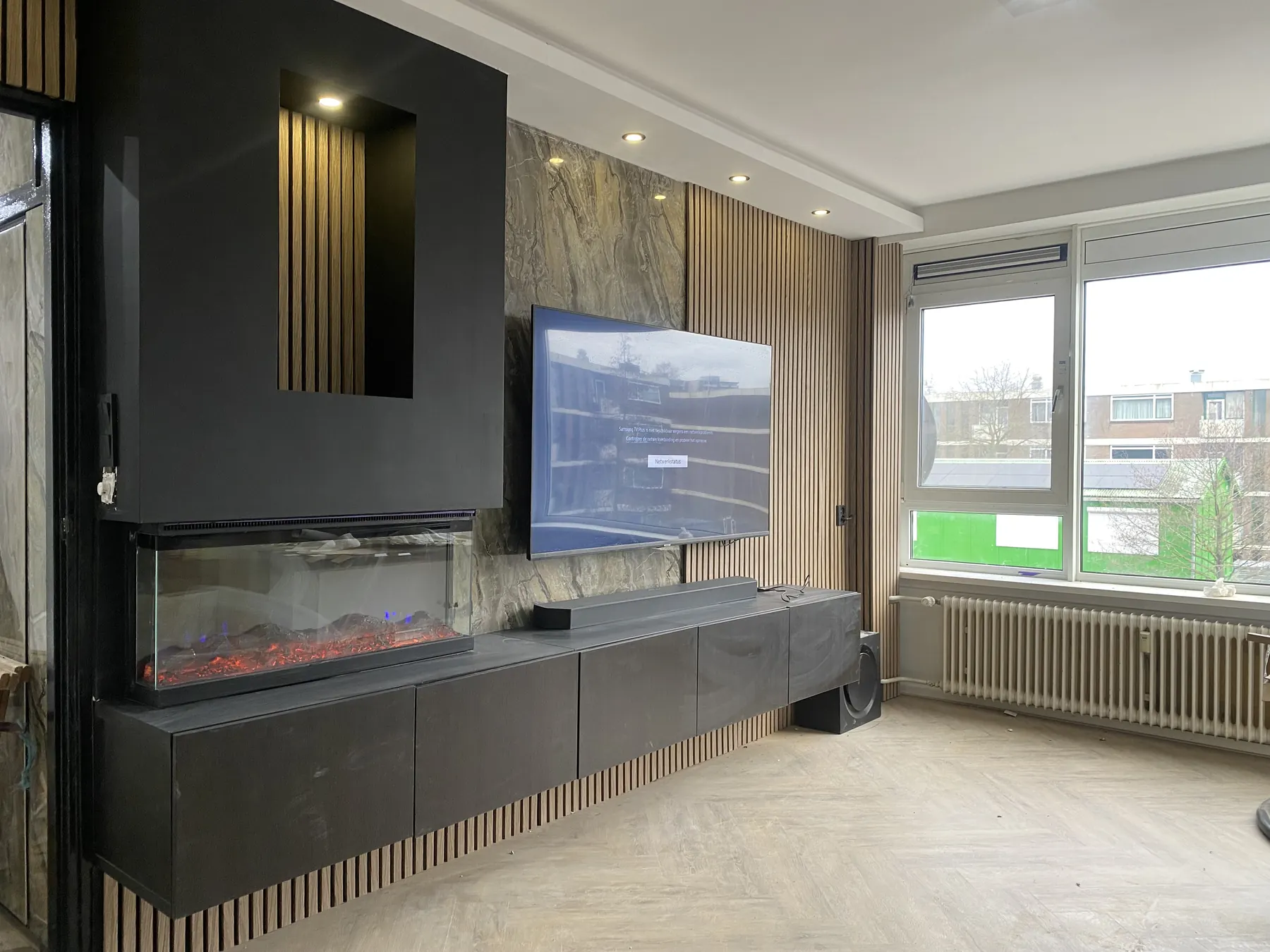 Luxe cinewall met donkergrijze kasten, houten latten, marmeren achterwand en ingebouwde sfeerhaard