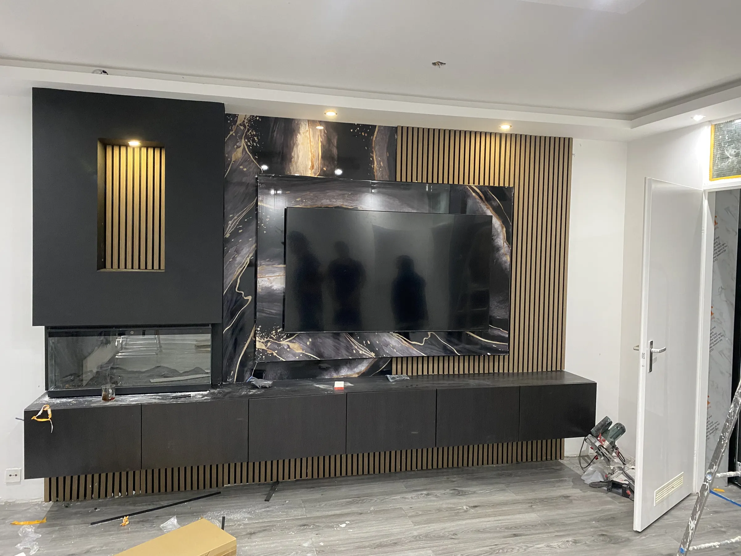 Exclusieve donkere cinewall met zwart marmeren look, gouden accenten, houten panelen en sfeerhaard